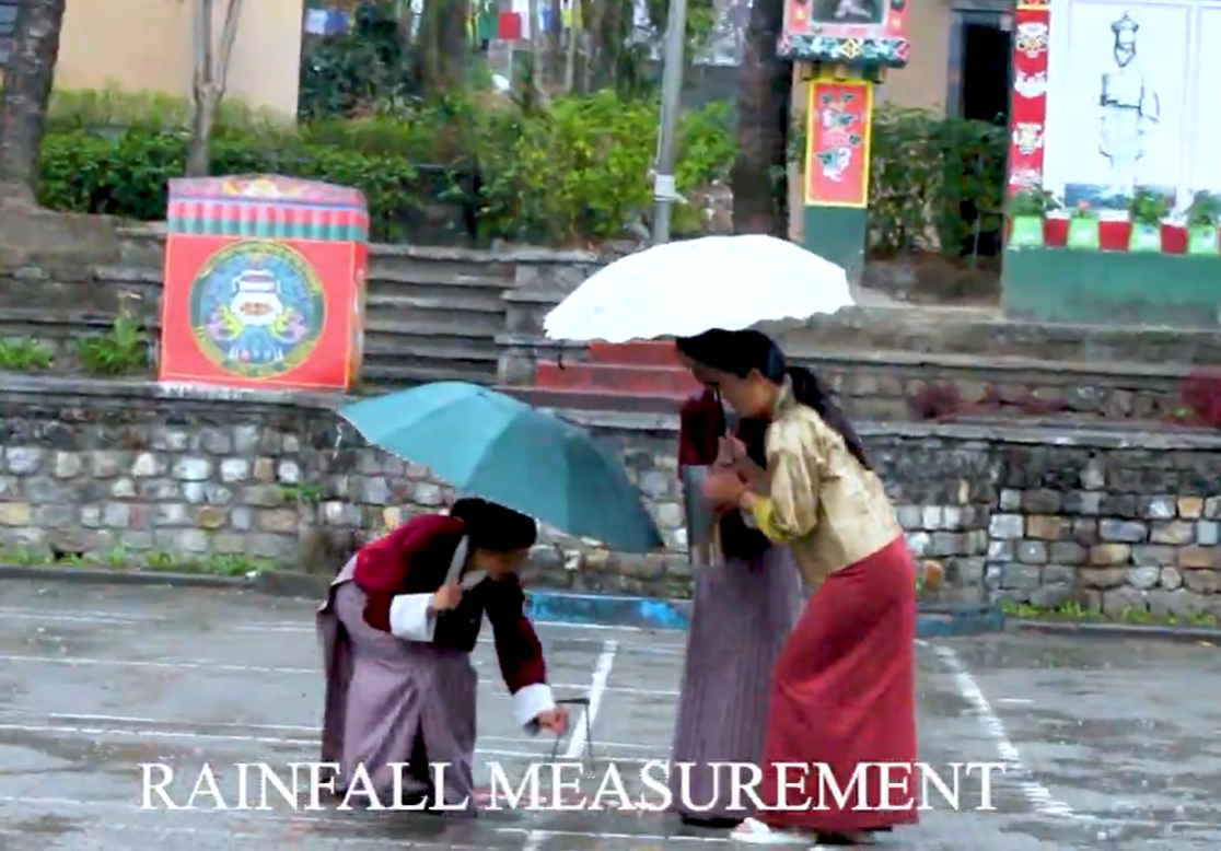 Female students in Bhutan standing holding umbrellas as they measure rainfall 