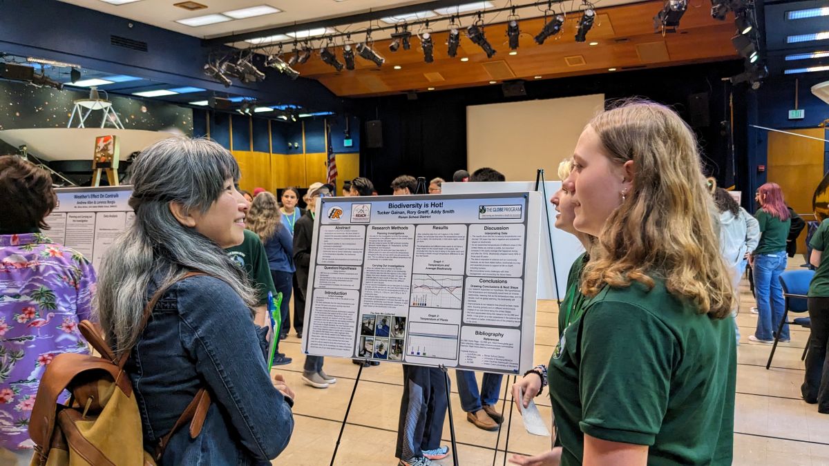 two students present their research poster to a STEM reviewer